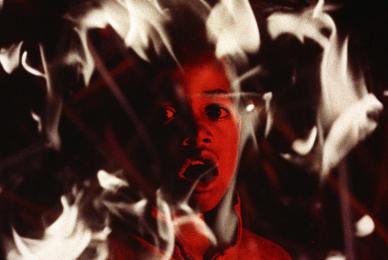young boy with red skin and mouth open engulfed in flames 